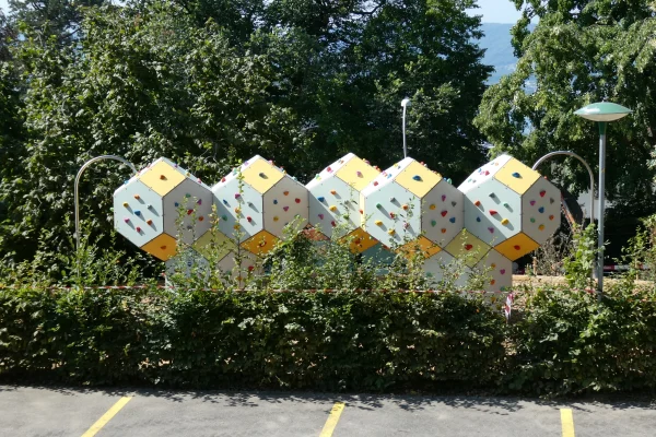 vue-ensemble-paysage-grimpe-cube-bloc Installation modulaire de bloc et de grimpe en extérieur avec corps de grimpe polygonaux, prises d’escalade colorées et protection contre les chutes en copeaux de bois.