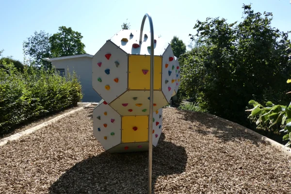 vue-face-paysage-grimpe-cube-bloc Installation modulaire de bloc et de grimpe en extérieur avec corps de grimpe polygonaux, prises d’escalade colorées et protection contre les chutes en copeaux de bois.